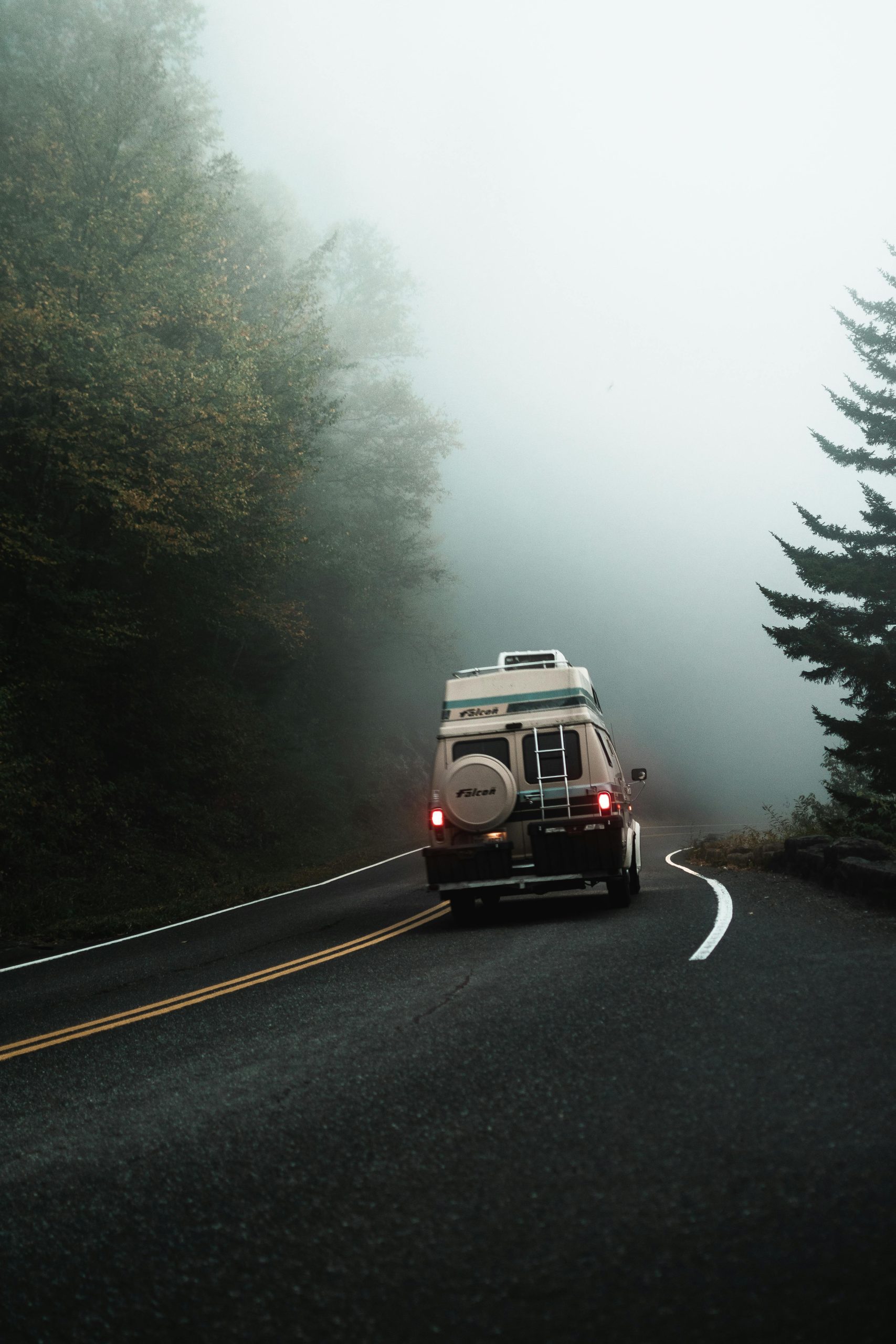A camper van travels through a foggy rural road, creating a serene scene for adventure.